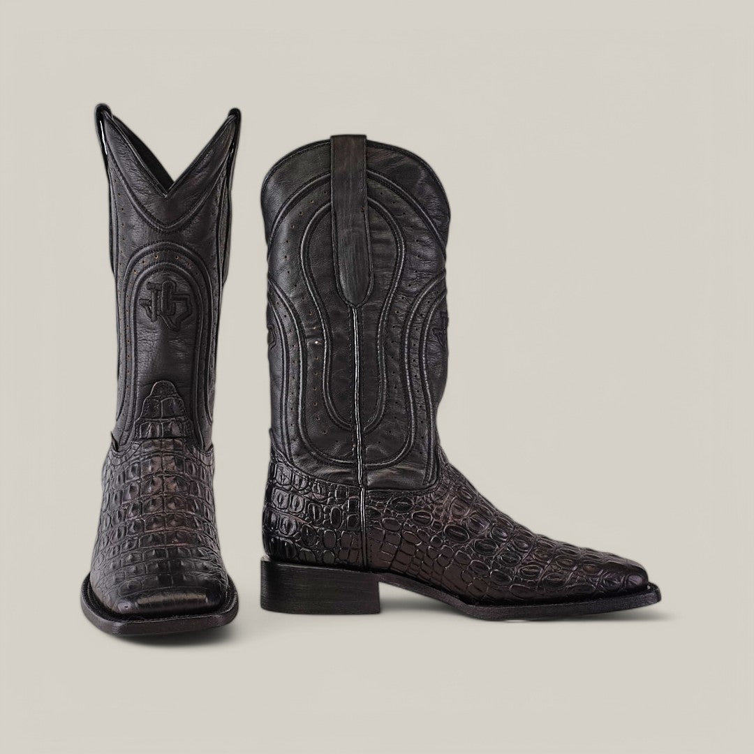 The Alligatoar Horn Back Print Black boots boast a square toe and intricate stitching with a decorative emblem on the shaft, highlighting exceptional leather craftsmanship with a crocodile pattern.