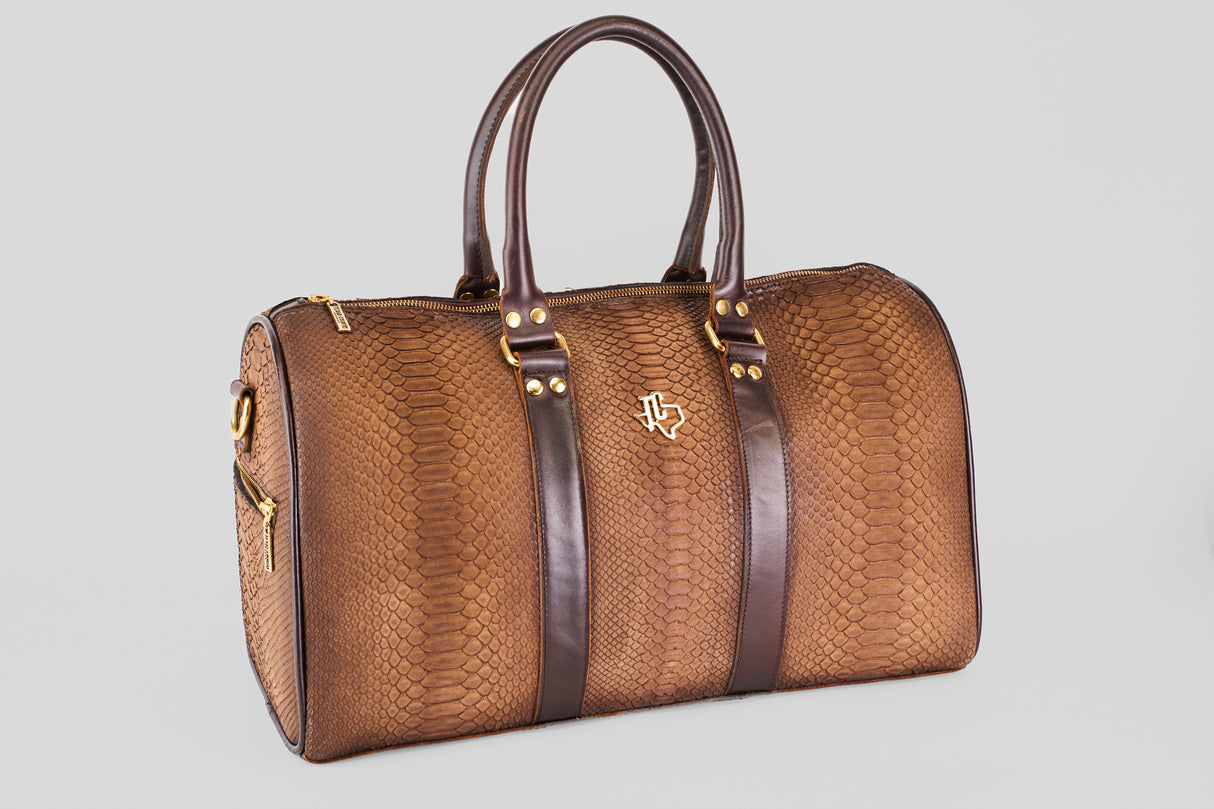 The Exotic Full Quilt Python - Tamarindo Travel Bag features brown leather with a snakeskin pattern, dark brown handles and straps, gold hardware, and a small gold logo, all set against a plain light gray background.