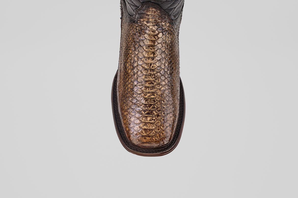 A close-up, top-down view of the Tanner Platinum - Dune - Square Toe (Imperial) boots shows their brown and gold python pattern, square toe, and dark stitching around the sole against a plain light gray background.