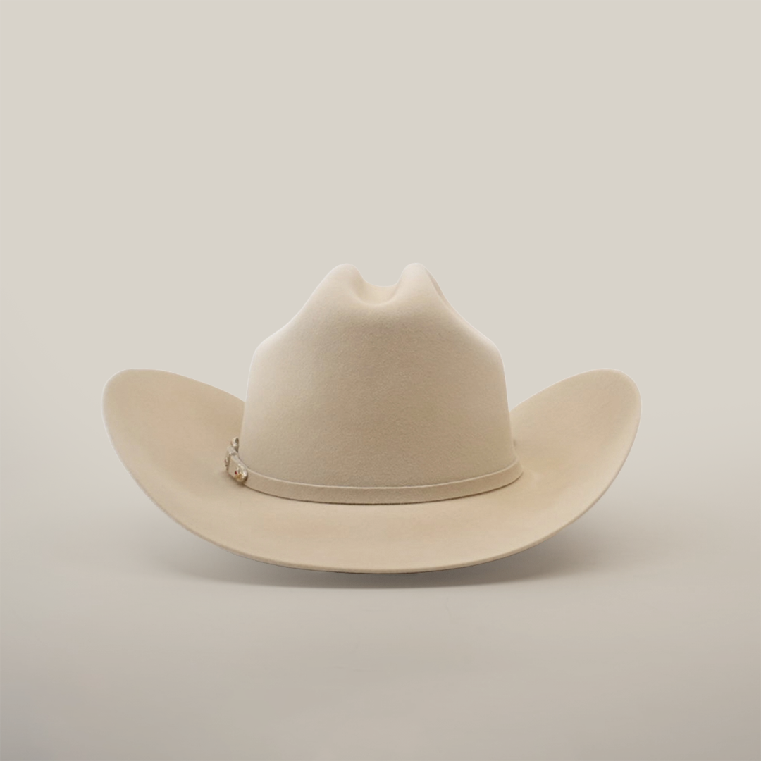 The 6X Real Belly is a beige fur felt cowboy hat with a wide brim and crease, set against a white background. It features a thin band with small decorative elements on the side, crafted from premium furs.