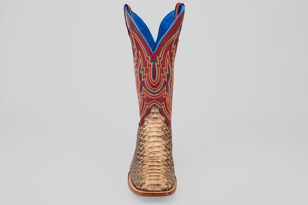 The Barlow - Taupe - Square Toe men’s statement boot features a textured taupe python leather lower, a vibrant red upper with blue and yellow stitching, and is displayed front-facing against a plain gray background.