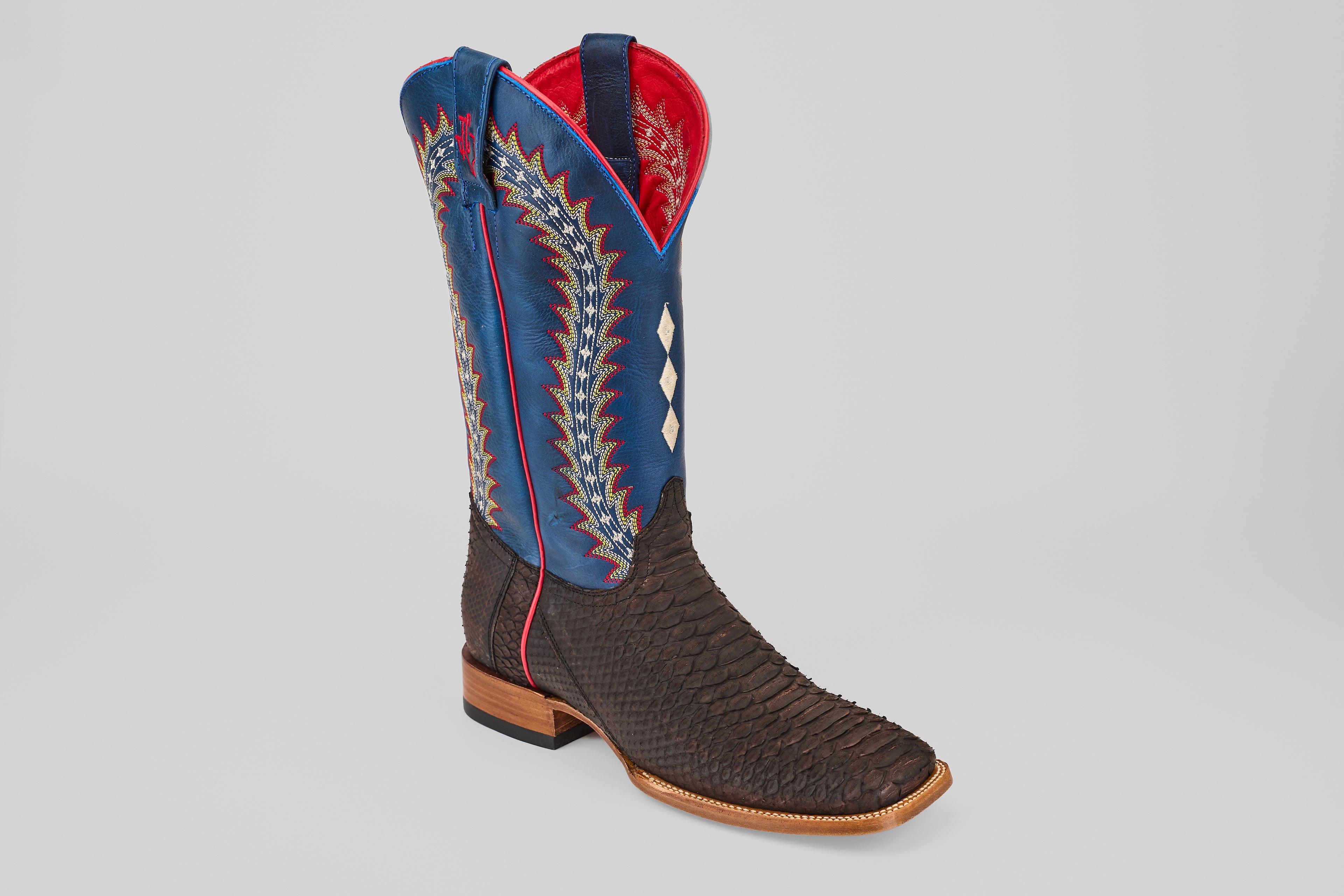 The Morgan - Matte Brown - Square Toe from the Diamond Collection showcases a dark brown textured foot, blue shaft, red trim, colorful zigzag stitching, white diamond inlays, and a classic wooden heel—perfect for men.