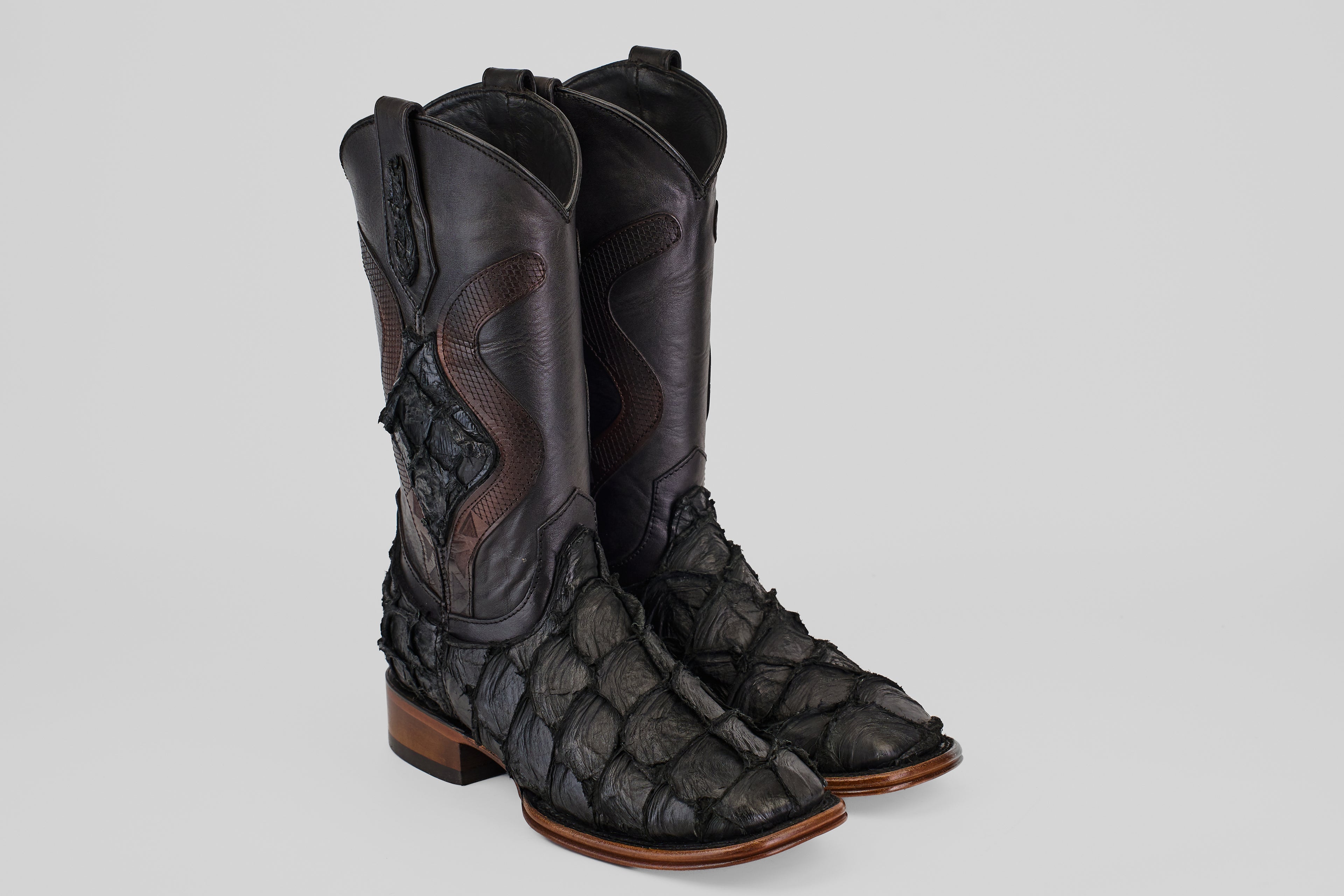 A pair of Conor Platinum - Matte Black - Square Toe (Diamond) boots with a textured, scale-like finish and brown wooden heels, displayed side by side on a light gray background.
