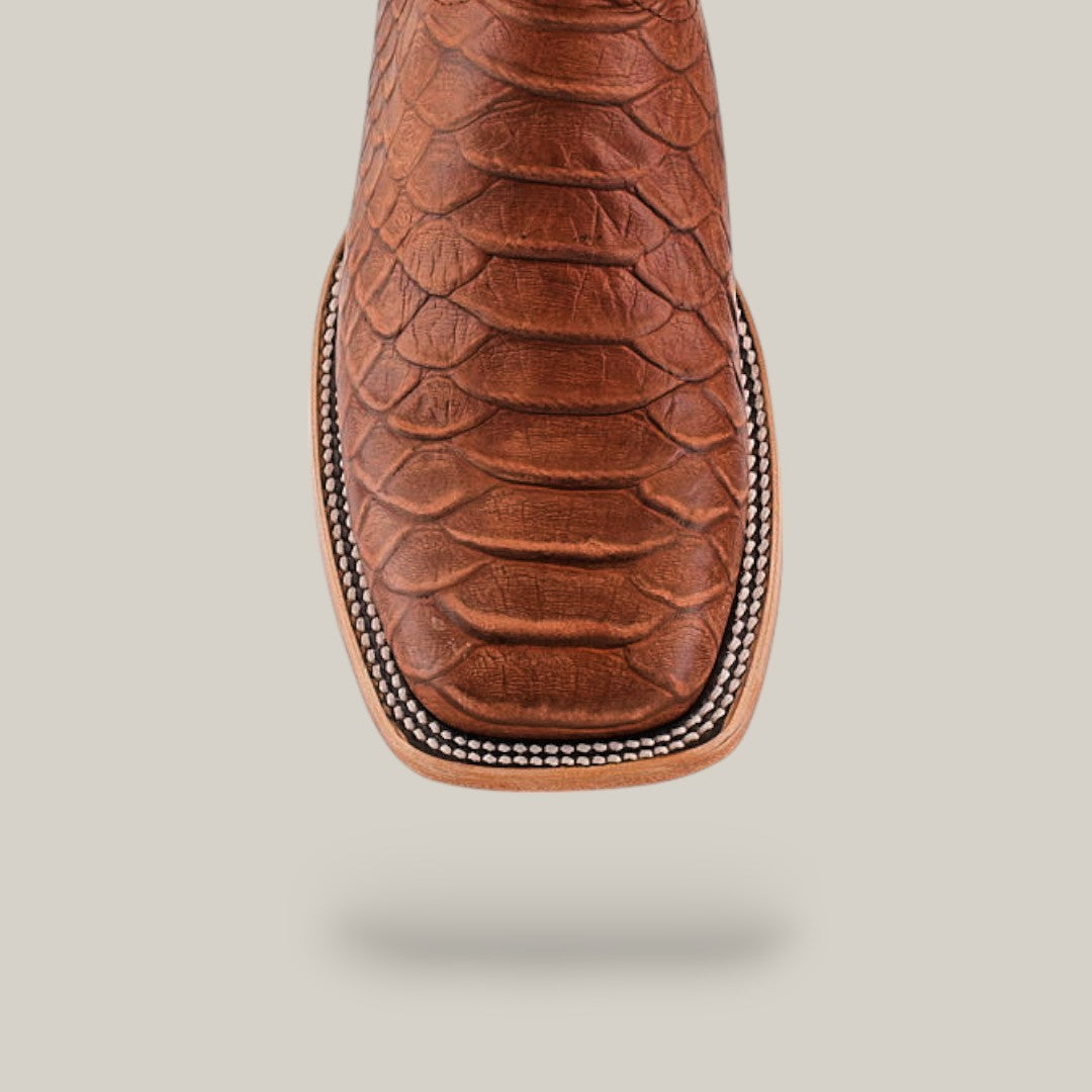 A close-up of the Python Print Rustic Cogñac - Square Toe boot, featuring a textured python print, cognac color, square toe, and white decorative stitching along the edge.