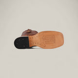 The Python Print Rustic Cogñac - Square Toe boot is shown from the bottom, displaying its tan sole with a stamped logo and a black heel section featuring visible nails.
