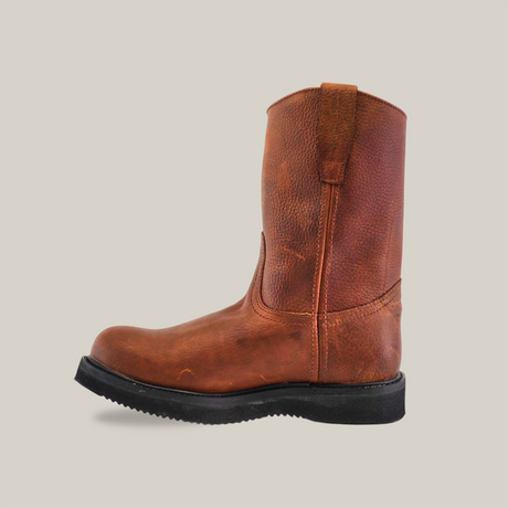 The Brandy Roper Laredo Sole brown leather pull-on work boot, shown from the side against a white backdrop, highlights its Western bootmaking roots with a rugged texture and black sole. Pull straps adorn the top for easy wearing.