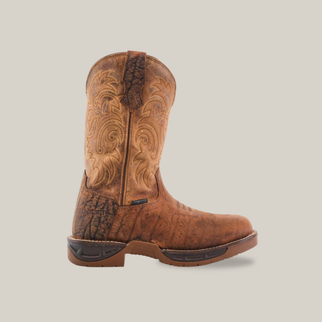 A Tan Brown Rough out boot, made from premium cowhide leather with decorative stitching and a rugged sole, is showcased on a white background. Its worn texture emphasizes its rustic style and the handcrafted excellence that makes it unique.